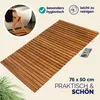 A wooden bath mat is shown next to a bathtub with a person's legs visible. Produktbild-Vorschau