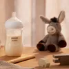 A baby bottle filled with milk is placed on a wooden surface next to a stuffed donkey toy and wooden blocks. Podgląd zdjęcia produktu