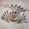 A collection of black cutlery arranged on a textured surface with a wooden disc. Anteprima dell’immagine prodotto
