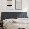 A close-up view of a dark gray upholstered headboard with a white pillow and a beige blanket on a bed. Produktbild-Vorschau