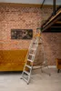 A ladder is placed in a room with a brick wall and a sofa. Náhľad obrázku produktu