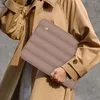 A person wearing a trench coat holds a brown laptop sleeve. Produktbild-Vorschau