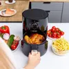 A person is holding an air fryer with a roasted chicken inside, surrounded by fresh ingredients and french fries. Produktbild-Vorschau