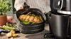 A person is holding an air fryer basket with cooked food inside, next to the air fryer appliance. Podgląd zdjęcia produktu