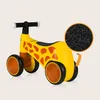 A yellow and orange giraffe-themed balance bike is shown against a light beige background. A circular inset shows a close-up of the black material of the wheels. Anteprima dell’immagine prodotto