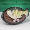 A novelty singing fish mounted on a plaque, set against a green wooden background. Produktbild-Vorschau