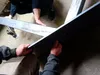 Two people are assembling a black metal table base with pre-drilled holes. Produktbild-Vorschau