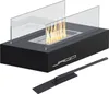 A black tabletop fireplace with glass wind guards and flames burning inside, shown with a black tool in front. Podgląd zdjęcia produktu