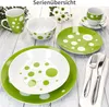 A collection of green and white polka dot ceramic tableware, including plates, bowls, and a mug, arranged on a light wooden surface. Voir les images du produit