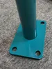 Close-up of the base of a teal-colored pole with a mounting plate and screw holes, resting on a gray, textured surface. Voir les images du produit