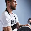 A man is shown performing bicep curls with a barbell while wearing a black arm blaster. Náhľad obrázku produktu