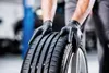 A person wearing black gloves is holding a car tire. Náhľad obrázku produktu
