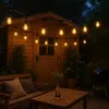 An outdoor patio scene at night, with string lights illuminating a wooden shed, bench, and table. Voir les images du produit