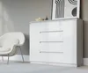 A modern white dresser with four drawers and two doors, placed next to a white armchair in a well-lit room. Voir les images du produit