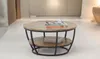 A round coffee table with a wooden top and black metal legs, placed in a modern living room setting. Produktbild-Vorschau