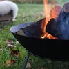 A close-up of a fire pit with burning logs in an outdoor setting with grass and fallen leaves. Produktbild-Vorschau