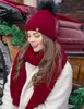 A woman wearing a red hat and scarf, smiling, with a carriage in the background. Voir les images du produit