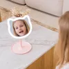 A young girl is looking into a pink cat-shaped makeup mirror with a light ring. Voir les images du produit