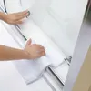 A person's hands are cleaning a glass shower door with a white towel. Produktbild-Vorschau