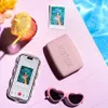 A pink Instax mini Link 3 printer, a smartphone displaying a photo, heart-shaped sunglasses, and a cocktail with a paper umbrella are arranged on a pink tiled surface next to a swimming pool. Anteprima dell’immagine prodotto