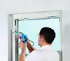 A man is using a caulking gun to seal a window frame. Produktbild-Vorschau