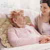 A young woman is talking to an elderly woman who is lying on an air mattress. Produktbild-Vorschau