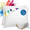 Two white pillows are shown against a white background, with colorful powder exploding from the top left. There are tags and a feather on the pillows. Náhled obrázku produktu