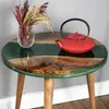 A round wooden and green resin coffee table with a red teapot and a vase of dried flowers. Produktbild-Vorschau