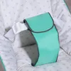 A close-up view of a teal-colored safety strap with a white buckle, attached to the interior of a baby bouncer or seat with a white fabric lining patterned with small gray hearts. Produktbild-Vorschau
