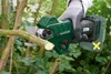 A gloved hand holds a cordless pruning shear, cutting a branch in a garden setting. Produktbild-Vorschau