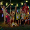 Children and an adult are sitting around a campfire at night, holding up a string of colorful LED lights shaped like astronauts, rockets, and planets. Náhled obrázku produktu