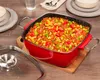 A red casserole dish filled with food, placed on a wooden cutting board on a wooden table. A glass lid and ladle are to the side. Produktbild-Vorschau