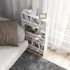 A white narrow shelving unit with items on it, placed next to a sofa and a window with sheer curtains. Podgląd zdjęcia produktu