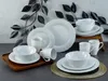 A collection of white porcelain dinnerware, including plates, bowls, and mugs, arranged on a wooden tray and a table. Náhľad obrázku produktu
