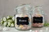 Two glass jars filled with colorful candies, placed on a surface with a bouquet of white flowers and meringue cookies. Produktbild-Vorschau