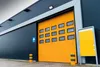 A large industrial garage door with multiple windows, set against the side of a dark gray building. Náhľad obrázku produktu
