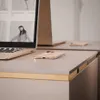 A desk with a laptop, two smartphones, and a second laptop in the background. Produktbild-Vorschau