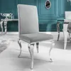 A grey velvet-look dining chair with silver legs is shown in a room with teal walls and a console table. Náhled obrázku produktu
