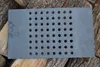 A rectangular cast iron grate with a grid of holes is placed on top of logs. Voir les images du produit