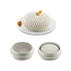 A white cake with a petal-like texture and gold decoration on top, placed on a white plate. Next to the cake is a small brown pastry. Below the cake are two silicone molds, one empty and one with a similar petal-like texture. Produktbild-Vorschau