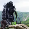 A backpack, hiking boots, and a solar-powered radio are set up on rocks in a mountainous landscape. Produktbild-Vorschau