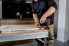 A person is using a cordless drill to attach a hinge to a piece of wood on a workbench. Anteprima dell’immagine prodotto