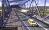 A view of a bridge with trucks and cars on it, with trees and houses in the background. Produktbild-Vorschau