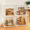 Four miniature dollhouse displays are shown inside clear acrylic boxes, arranged in a 2x2 grid on a wooden surface. Podgląd zdjęcia produktu