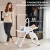 A woman stands next to a baby high chair with a baby in it, in a modern home setting. Produktbild-Vorschau