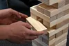 A close-up shot of hands playing Jenga, carefully removing a block from the tower. Produktbild-Vorschau