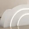 A close-up view of a modern, white reception desk with curved sections and integrated LED lighting. Produktbild-Vorschau