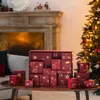 An advent calendar is displayed on a wooden table in front of a fireplace and a Christmas tree. Produktbild-Vorschau