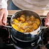 A person is holding a pot of food cooking on a stovetop. Produktbild-Vorschau