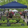 People browsing plants at an outdoor market under a blue canopy. Produktbild-Vorschau